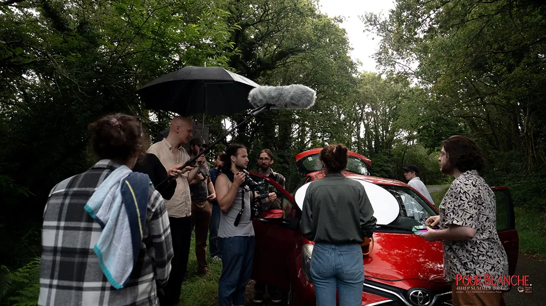 L'équipe de tournage est rassemblée sous la pluie autour d'une voiture rouge